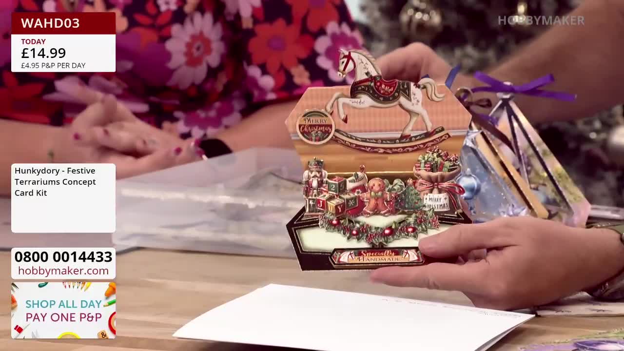 A person holds up a festive card kit from Hobby Maker, showcasing a pop-up Christmas scene with a rocking horse and other decorations. The price is displayed on the screen, and the telephone number is visible for viewers in the United Kingdom.
