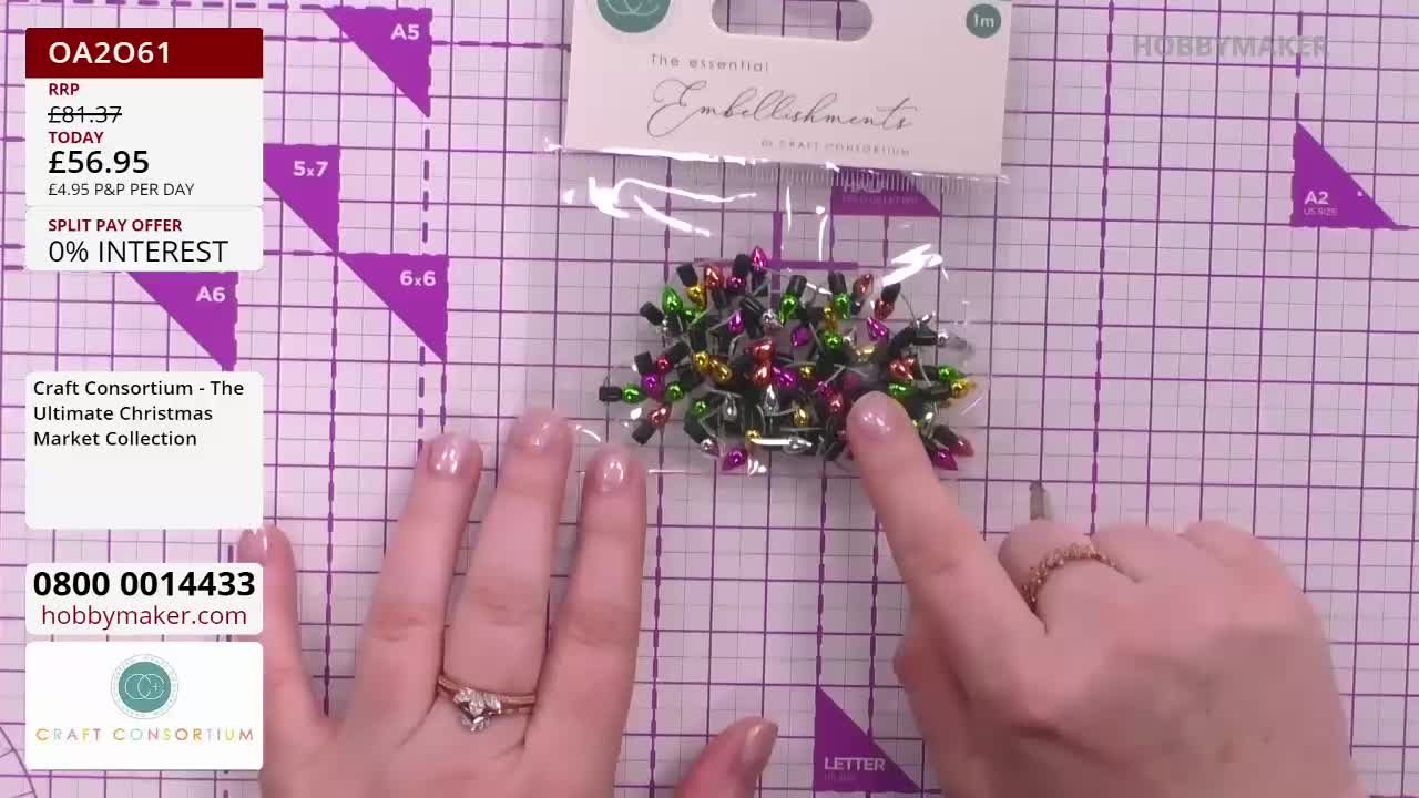 A hand is pointing to a packet of miniature Christmas light embellishments, showcasing them on a Hobby Maker cutting mat. The on-screen price is displayed, and the Craft Consortium collection is being promoted.
