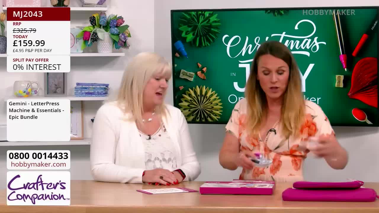 A woman in a floral top holds small, colorful items, gesturing with them as she speaks. Beside her, another woman in a white cardigan looks on, also speaking, while a screen behind them advertises a product from Hobby Maker.
