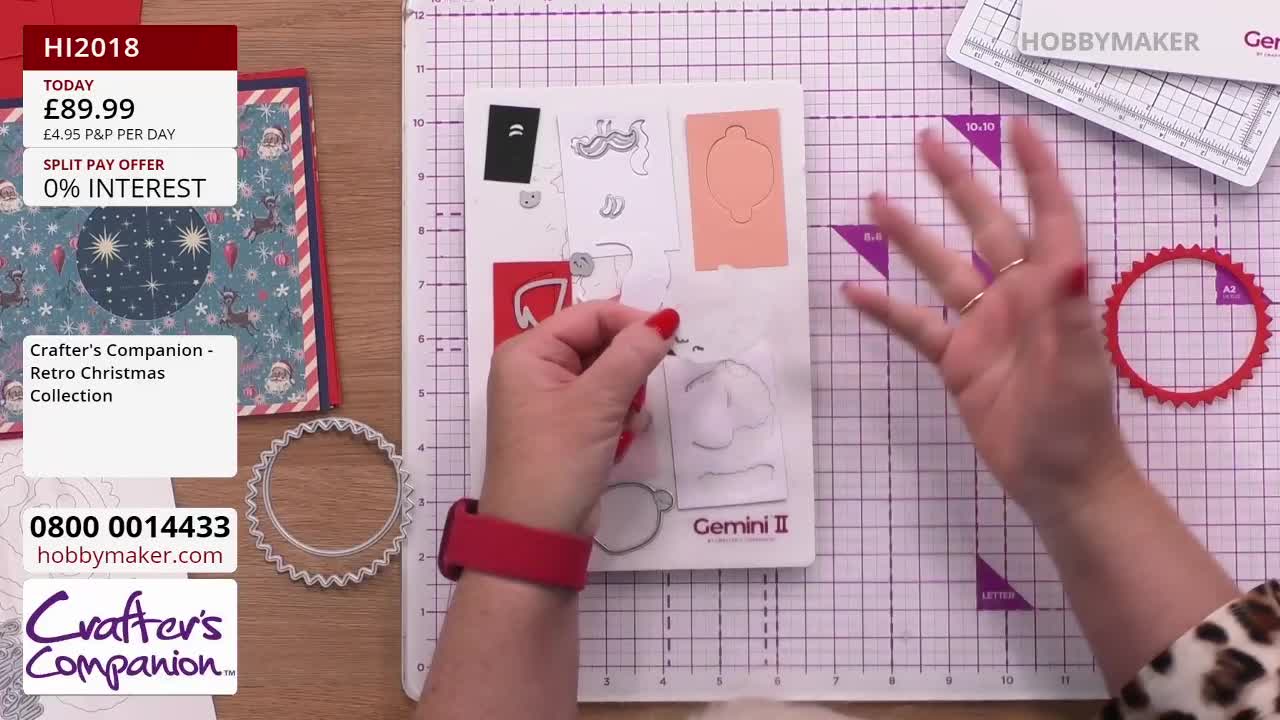 A woman with red nail polish holds a small paper shape, gesturing with her other hand towards a red, circular die-cut. The Hobby Maker presentation is showcasing a Christmas craft project, with the Crafter's Companion collection details visible.

