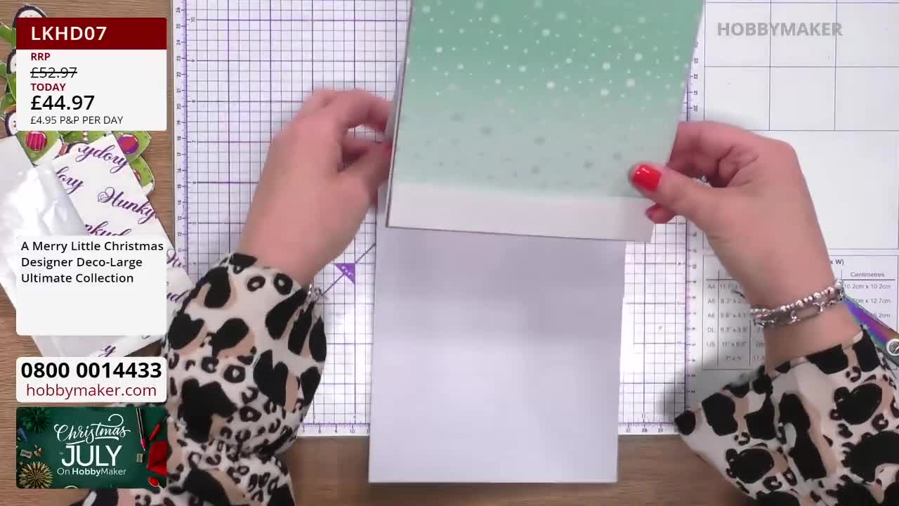 A woman holds a card decorated with a snowy scene over a blank white one. She's likely demonstrating a craft project on Hobby Maker.
