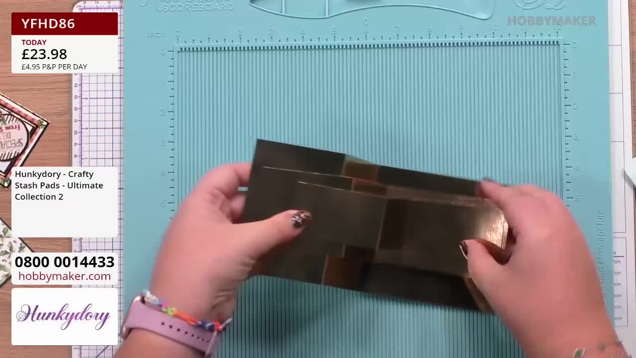 A person holds a stack of shiny, dark gold cardstock. The Hobby Maker scoring board sits beneath, ready for the next step.

