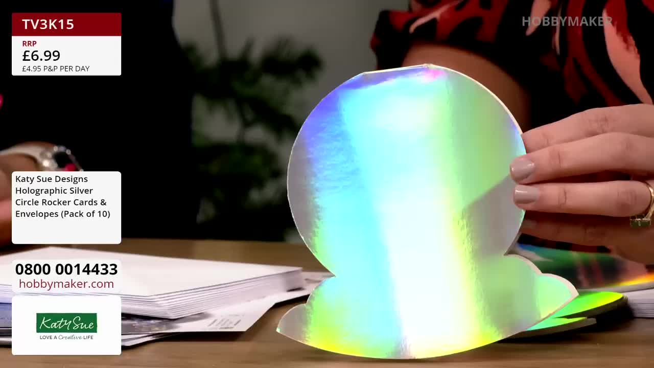 A hand holds up a large, iridescent card, shaped like a circle with a cloud-like design at the bottom. The Hobby Maker logo is visible in the upper right corner, and the price of the "Holographic Silver Circle Rocker Cards" is displayed on the screen.
