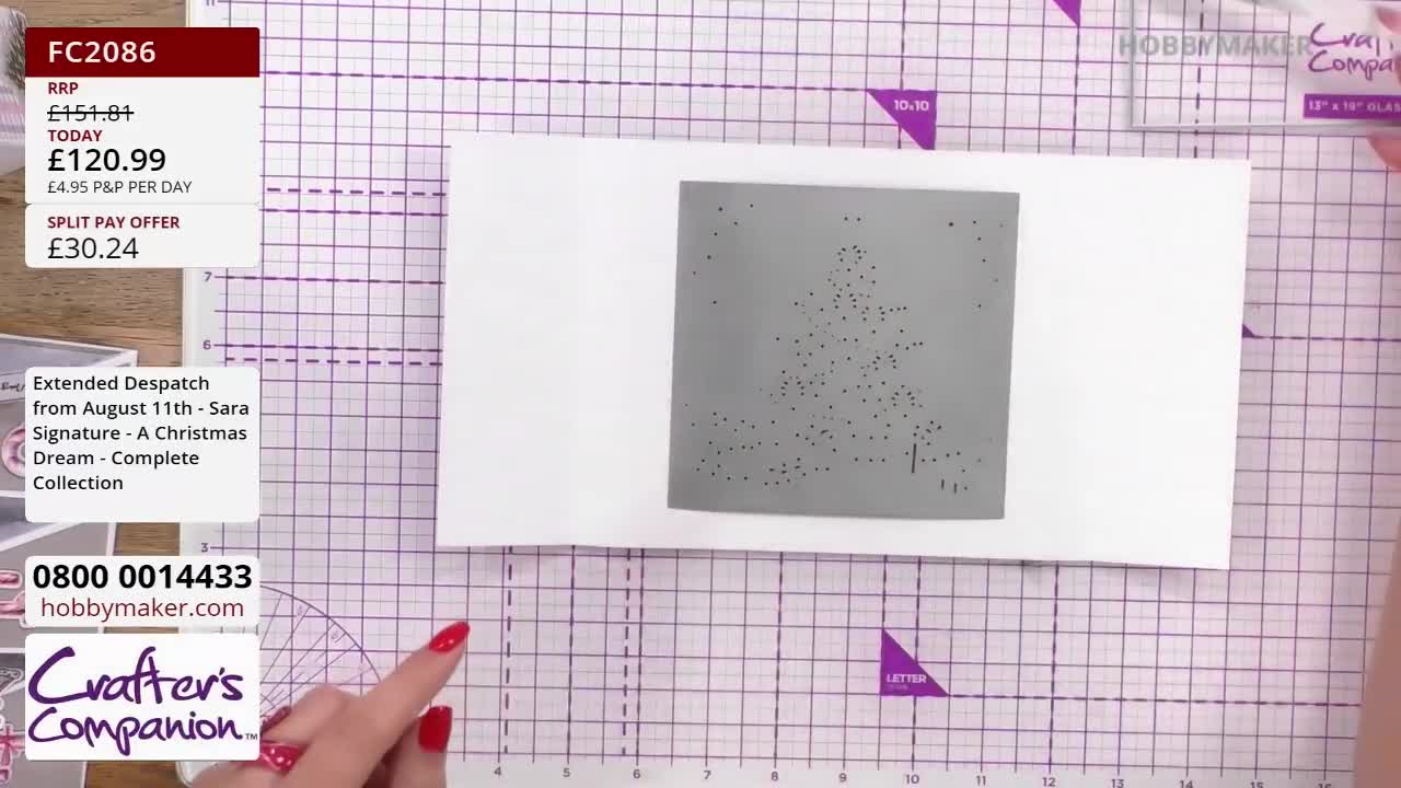A gray stencil with a Christmas tree design sits on a white card, ready for use. A hand, with red nail polish, points to the card on the Hobby Maker cutting mat.
