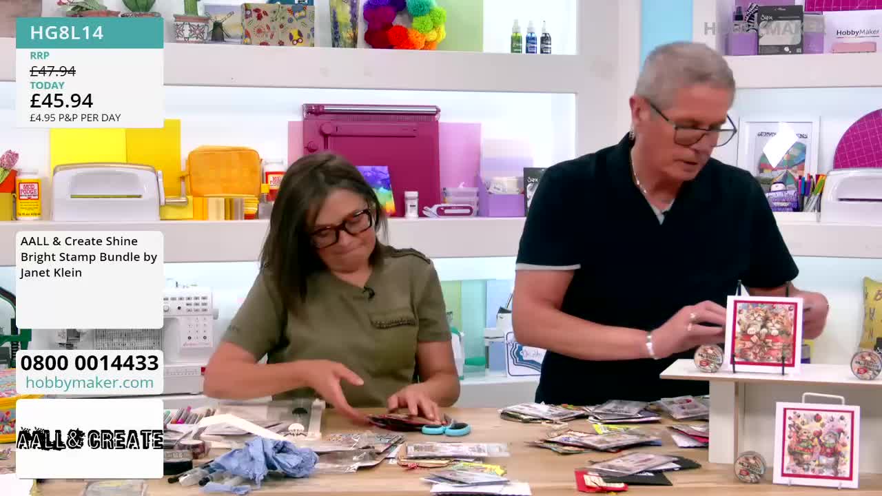 A woman in glasses sorts through a pile of small, shiny items, while a man adjusts a framed piece of artwork. The scene appears to be a crafting demonstration, likely for Hobby Maker in the United Kingdom.
