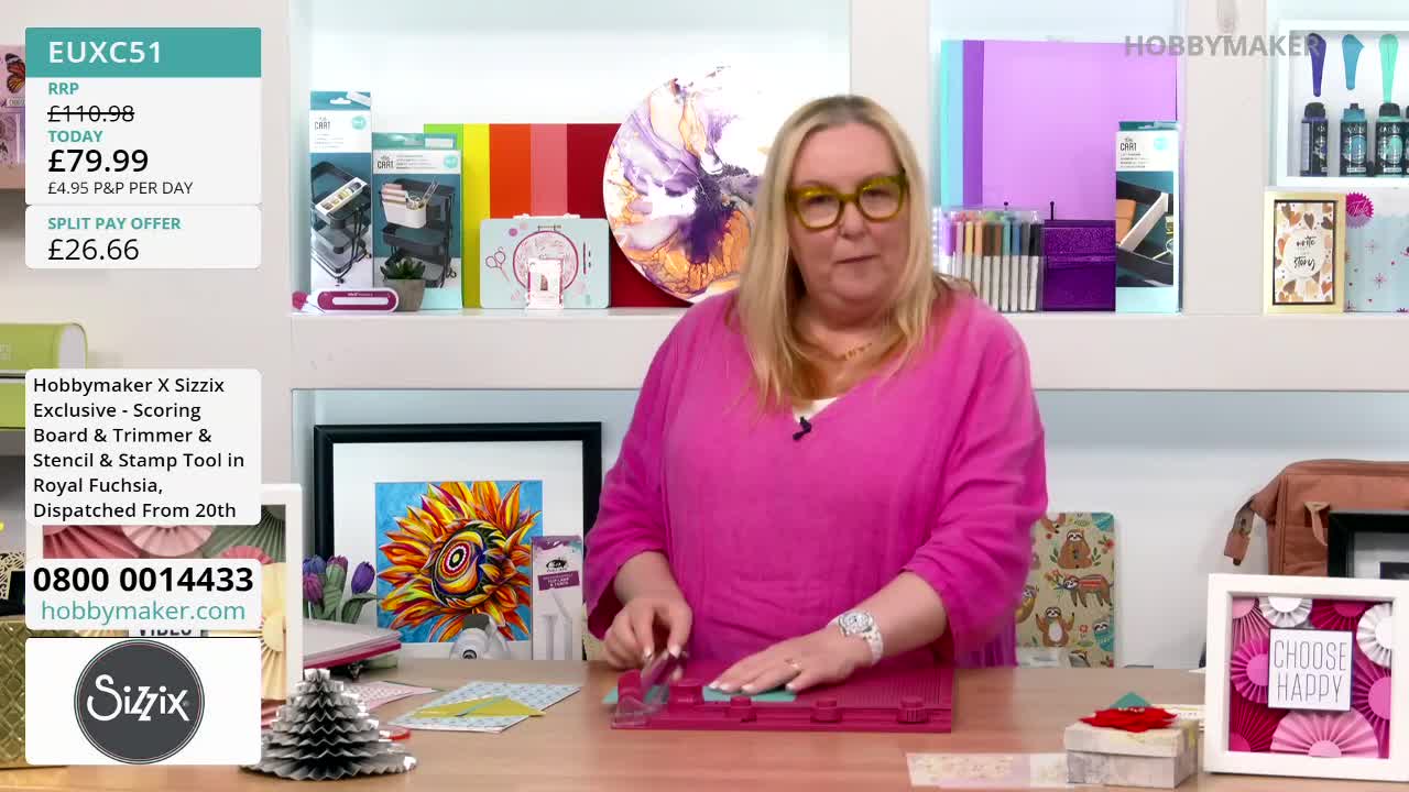 A woman in a pink top, wearing glasses, uses a scoring tool on a pink cutting board. She's demonstrating a craft product from Hobby Maker, likely for a United Kingdom audience.
