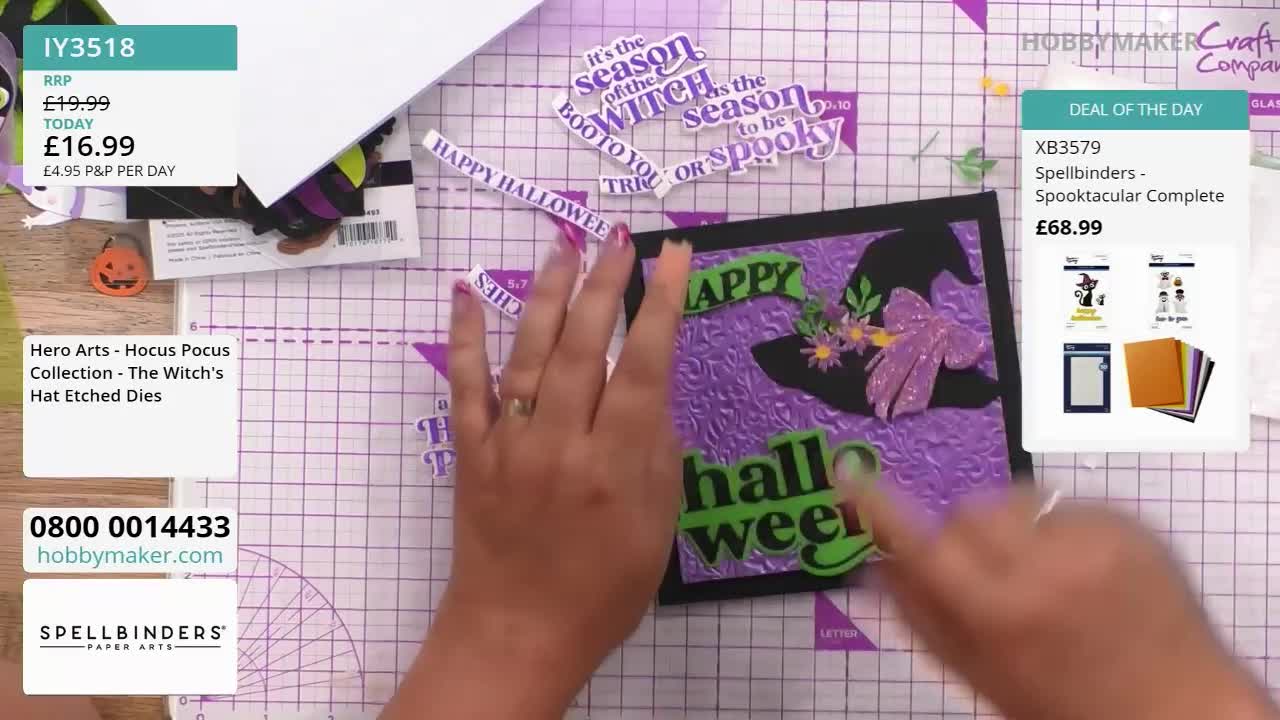 A hand is arranging die-cut Halloween-themed words and shapes onto a textured purple card. The Hobby Maker logo is in the background, and a deal of the day is advertised on the right.
