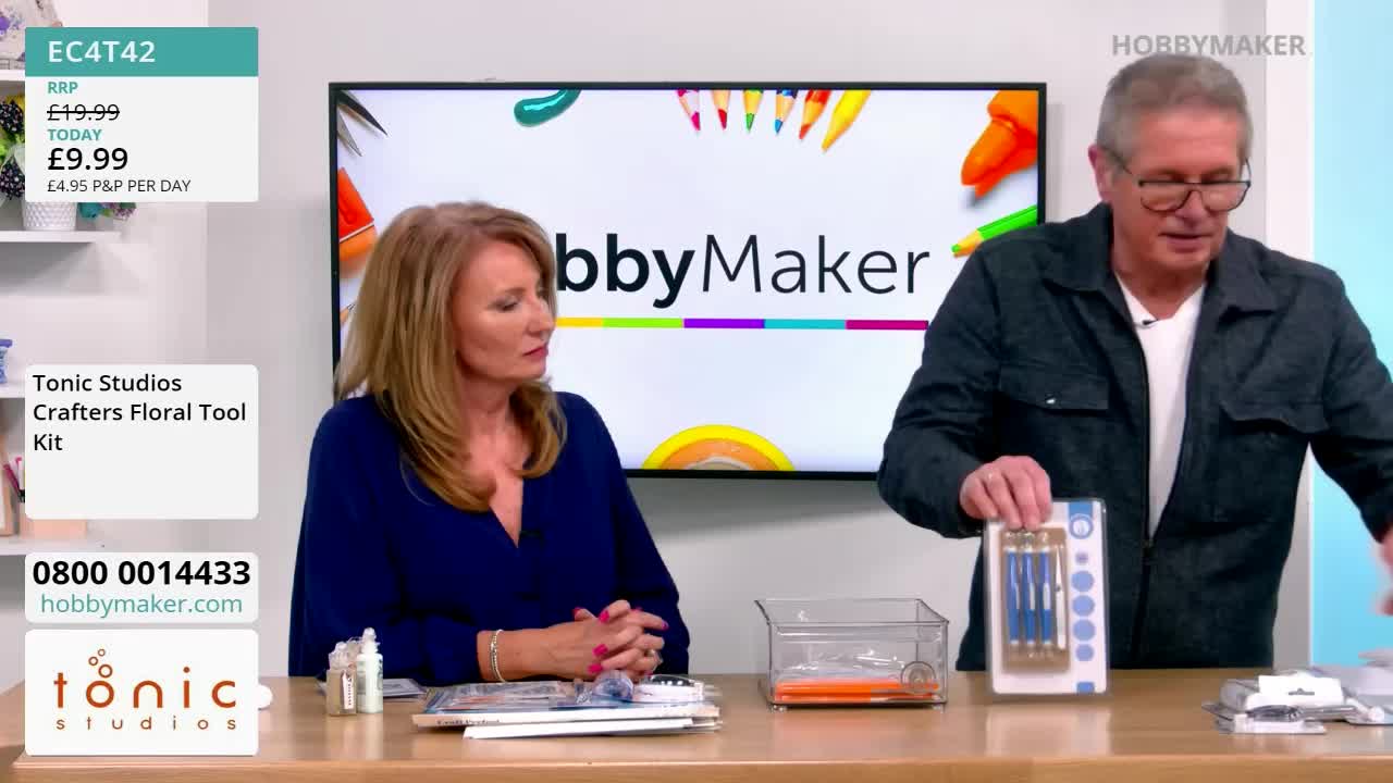 A man in glasses holds up a package of tools, while a woman looks on. The Hobby Maker logo is visible on the screen behind them.
