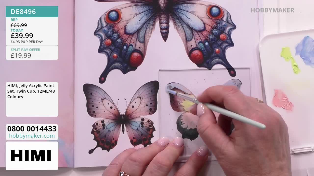 A hand, holding a thin brush, carefully applies light blue paint to a butterfly wing. Beside it, a palette holds dabs of pink, yellow, and blue, all from the Hobby Maker set.
