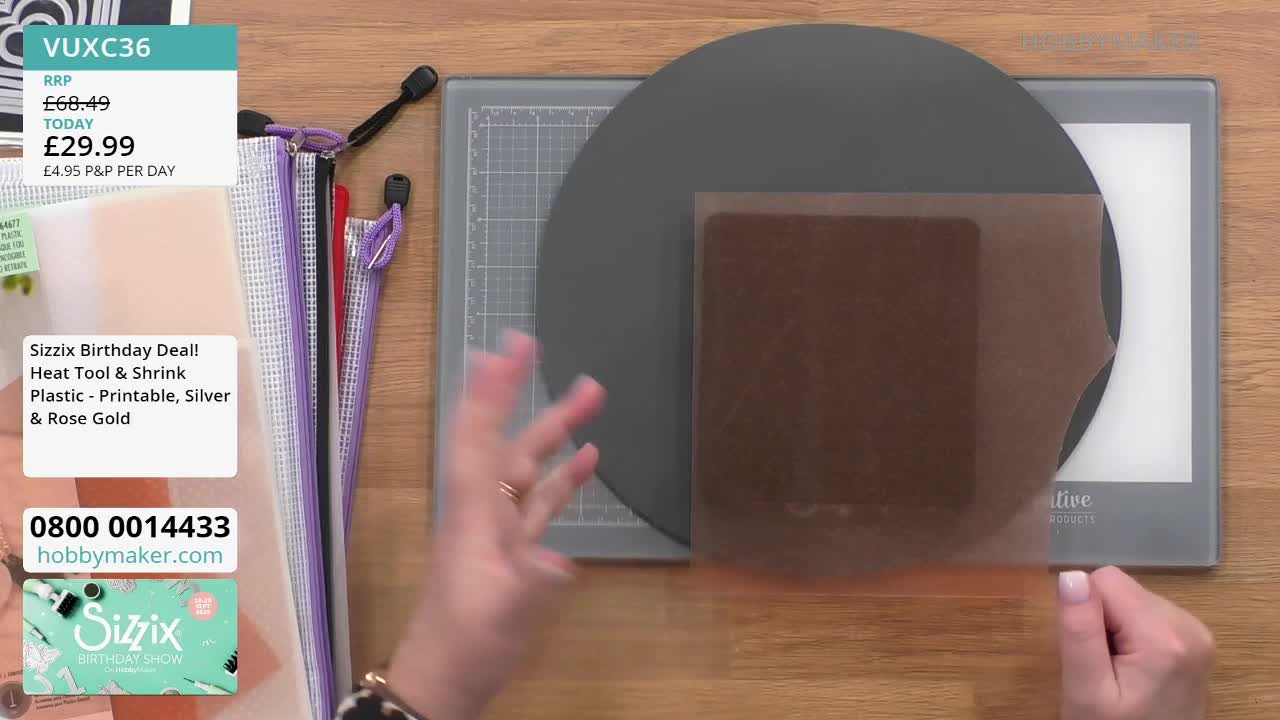A woman's hands are gesturing over a dark gray circle and a light-up craft pad. A square piece of brown plastic sits on top of the pad, possibly for a Hobby Maker craft demonstration.
