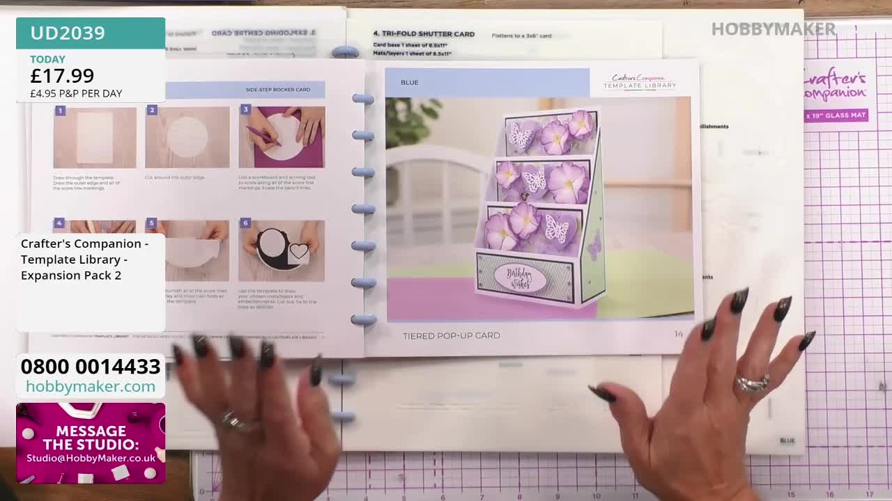 A woman's hands frame an open book showcasing a tiered pop-up card, part of a Crafter's Companion template library. The Hobby Maker logo and a phone number are visible at the bottom of the screen.
A woman's hands frame an open book showcasing a tiered pop-up card, part of a Crafter's Companion template library. The Hobby Maker logo and a phone number are visible at the bottom of the screen.