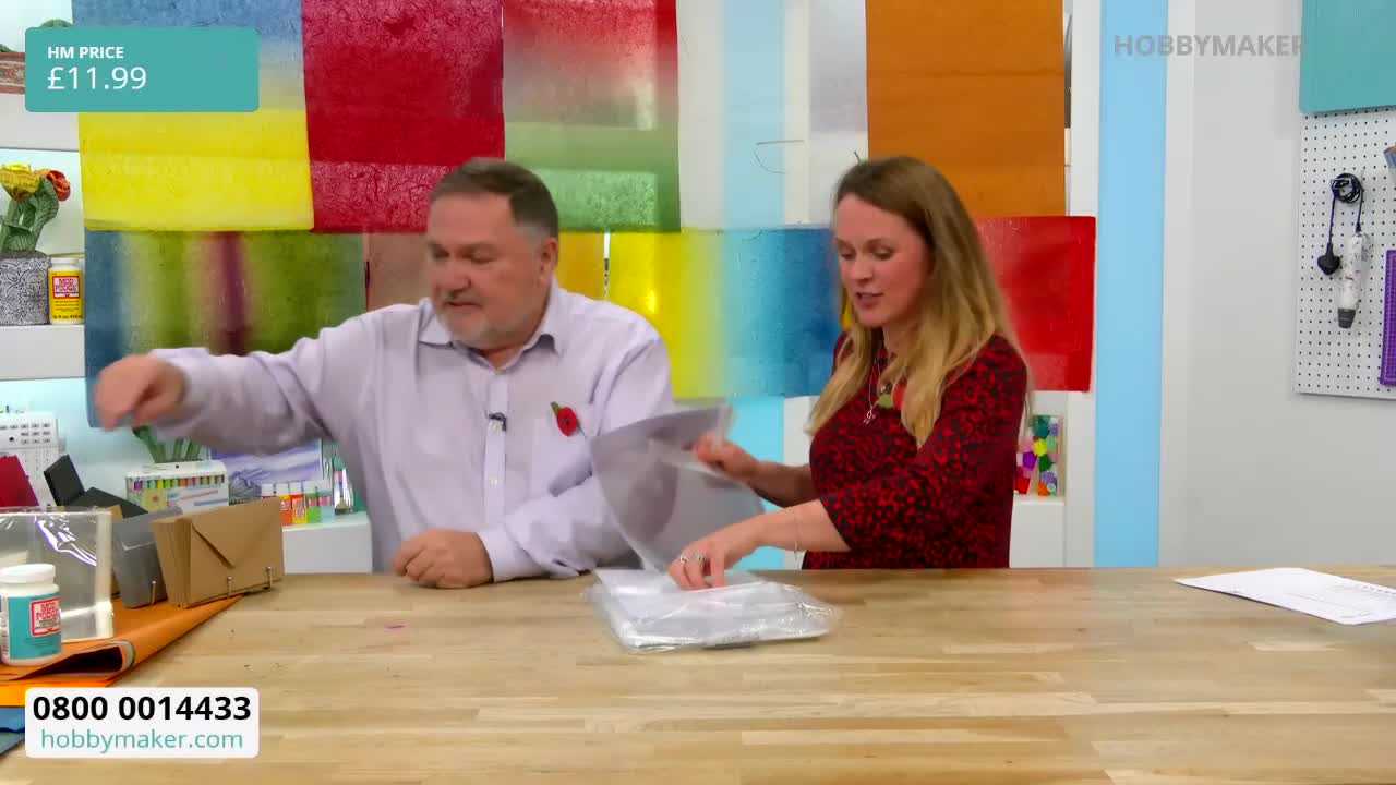 On a set for Hobby Maker, a woman in a red top is pulling items from a clear plastic bag. The man beside her points towards the table, where various craft supplies are displayed.
On a set for Hobby Maker, a woman in a red top is pulling items from a clear plastic bag. The man beside her points towards the table, where various craft supplies are displayed.