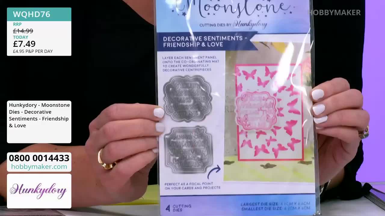 A person's hands display a package of "Moonstone" cutting dies from Hobby Maker, featuring decorative sentiments. The package shows a sample card with pink butterfly accents and a framed sentiment.
