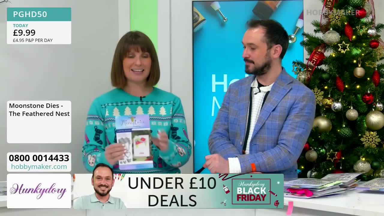 A woman in a festive sweater holds up a craft product, smiling at the camera. Beside her, a man in a blue blazer looks on as they present the item during a Hobby Maker segment.
