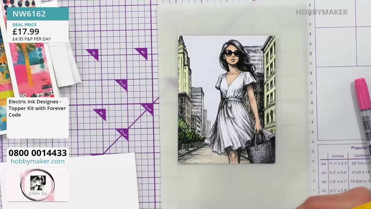 A woman in a white dress is drawn on a card, set against a cityscape.  A pink marker rests nearby on a Hobby Maker surface, ready for use.
