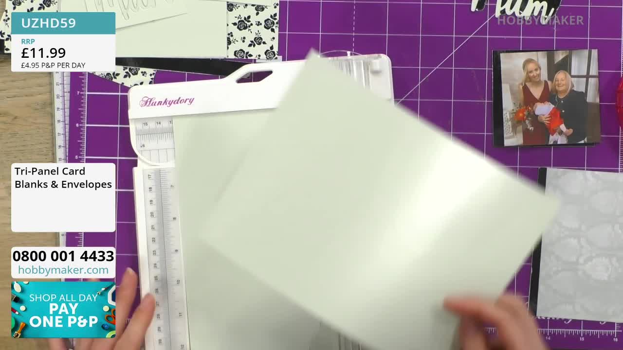 A pale green card is being slid into a white cutting machine. The cardstock is positioned over a purple mat with grid lines.