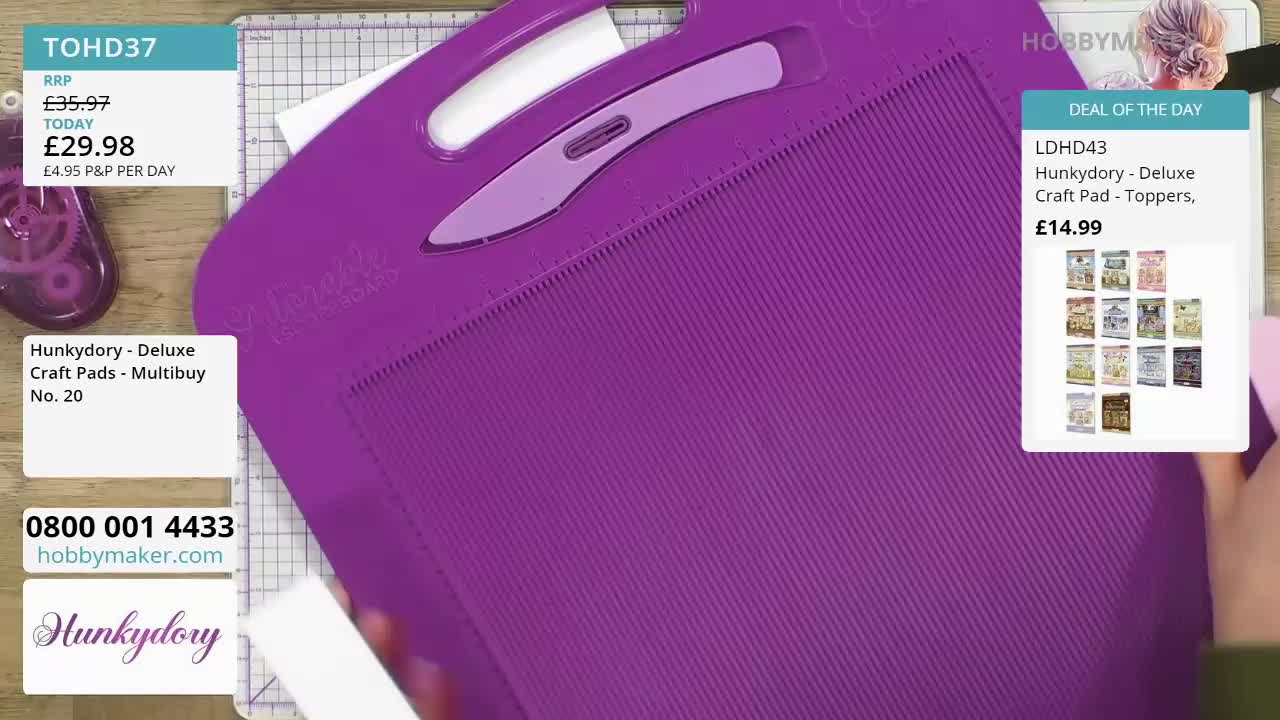 A large purple crafting tool is being held over a white surface. A hand is reaching in from the right to adjust the tool.