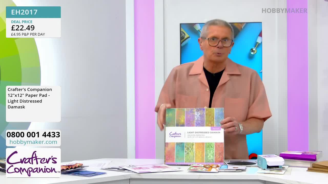 A man in a peach shirt holds up a paper pad featuring various distressed damask patterns. He's on a set for HobbyMaker, a UK craft channel.
