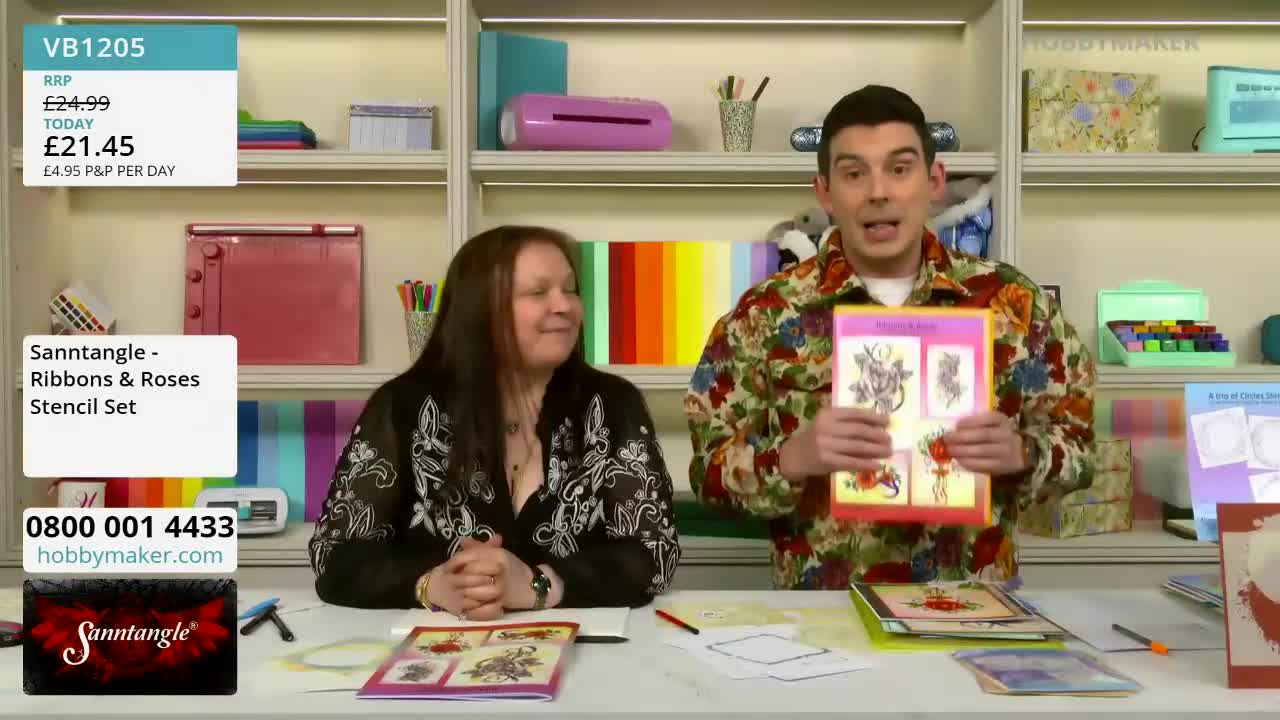 A man in a colourful shirt holds up a stencil set, talking enthusiastically. Beside him, a woman with long dark hair smiles, her hands clasped on the table.