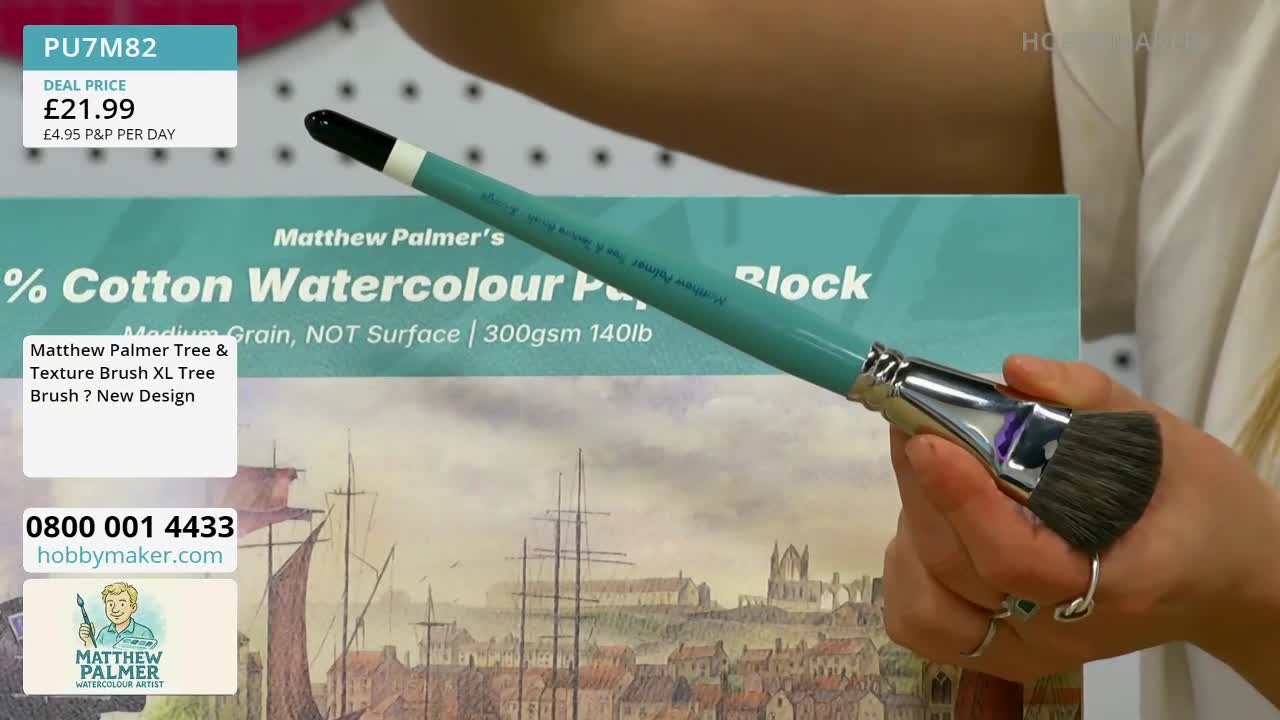 A hand holds a teal paintbrush with a silver ferrule, its bristles dark and dense. Behind it, a block of Matthew Palmer's 100% Cotton Watercolour Paper is displayed, showing a detailed watercolour of a coastal town.