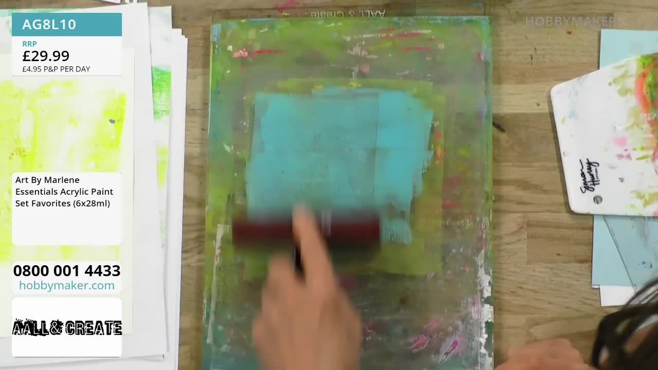 A hand rolls a brayer across a gel plate, spreading a vibrant turquoise paint over a green background. The textured surface of the plate shows remnants of pink and yellow paint from previous applications.
