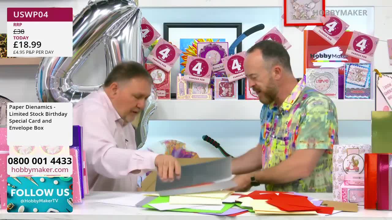 The man in the pink shirt is carefully placing a grey card into a box. Beside him, the man in the colourful shirt is looking down at a pile of paper.