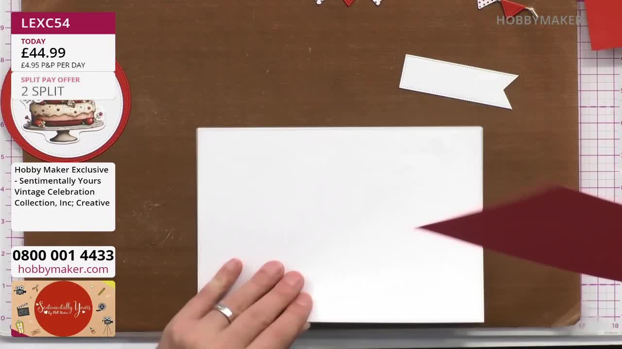 A hand with a silver ring is placing a piece of deep red cardstock onto a white card. A white banner shape with a gold edge sits above the card. A hand with a silver ring is placing a piece of deep red cardstock onto a white card. A white banner shape with a gold edge sits above the card.