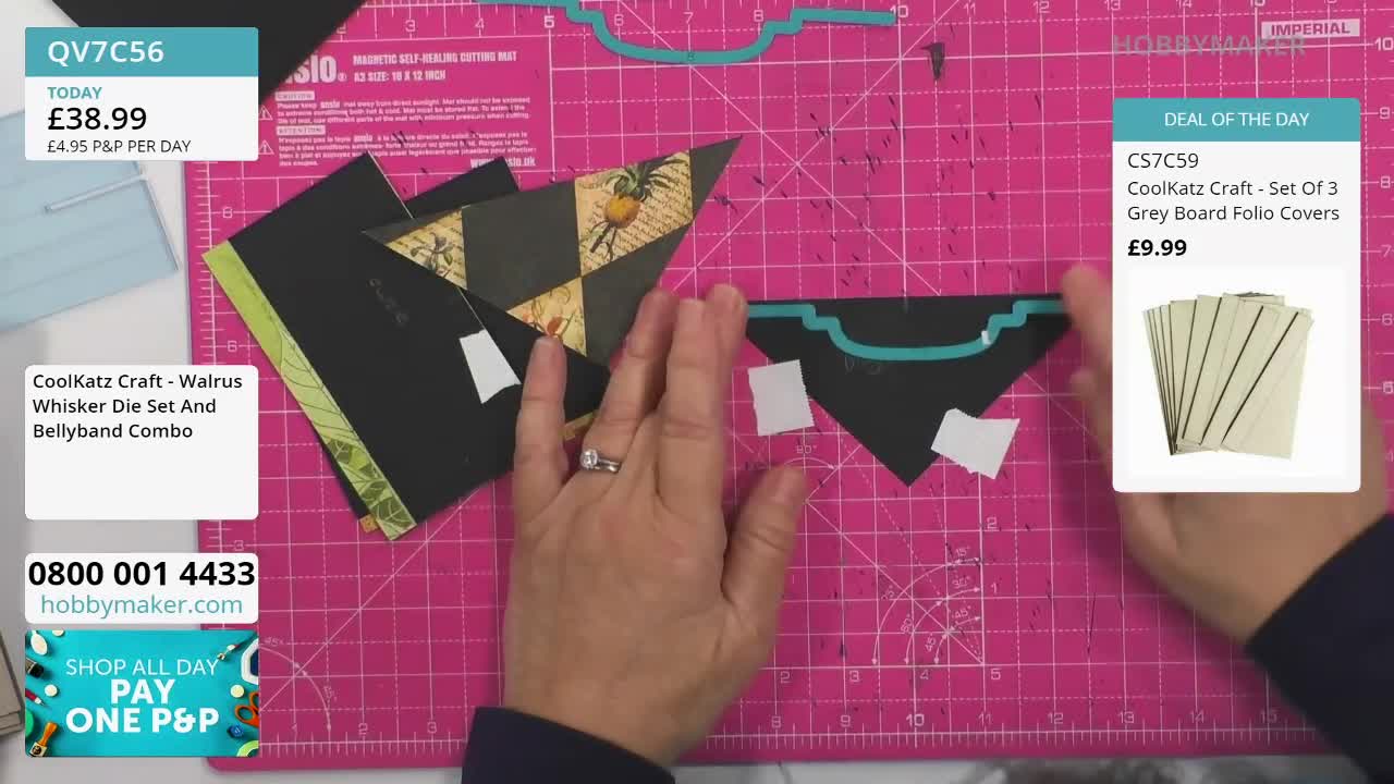 Hands arrange black cardstock cutouts on a pink cutting mat. A woman's fingers adjust a triangular piece patterned with pineapples and a checkered design.