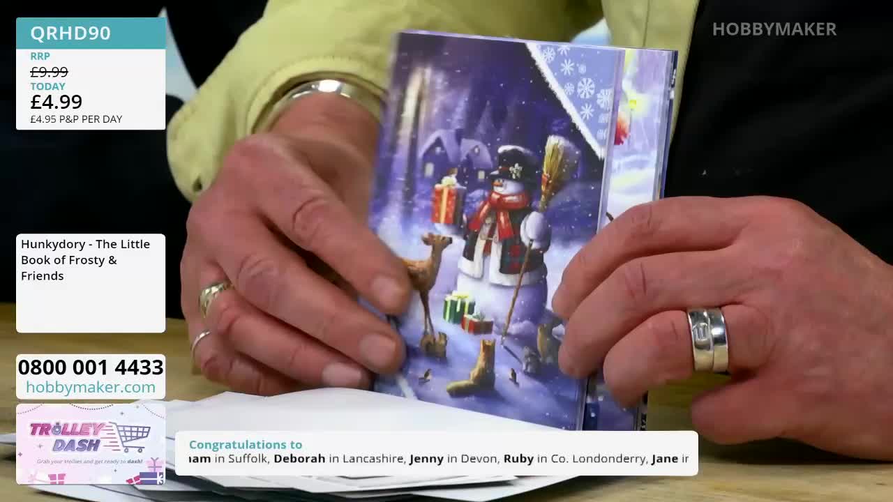 Fingers adjust a festive card featuring a snowman and reindeer. The Hobby Maker logo is visible on the screen.