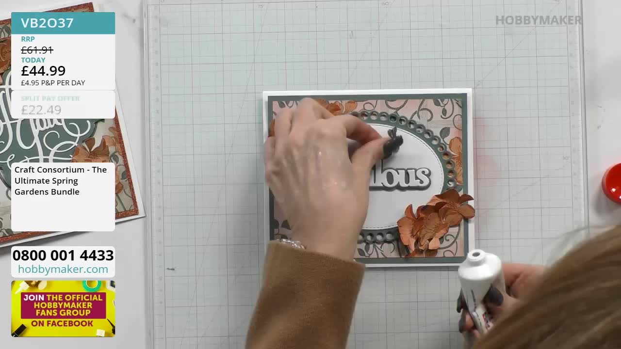 Fingers carefully place a small, dark embellishment onto a handmade card. A tube of glue sits ready for the next step in this crafting project.