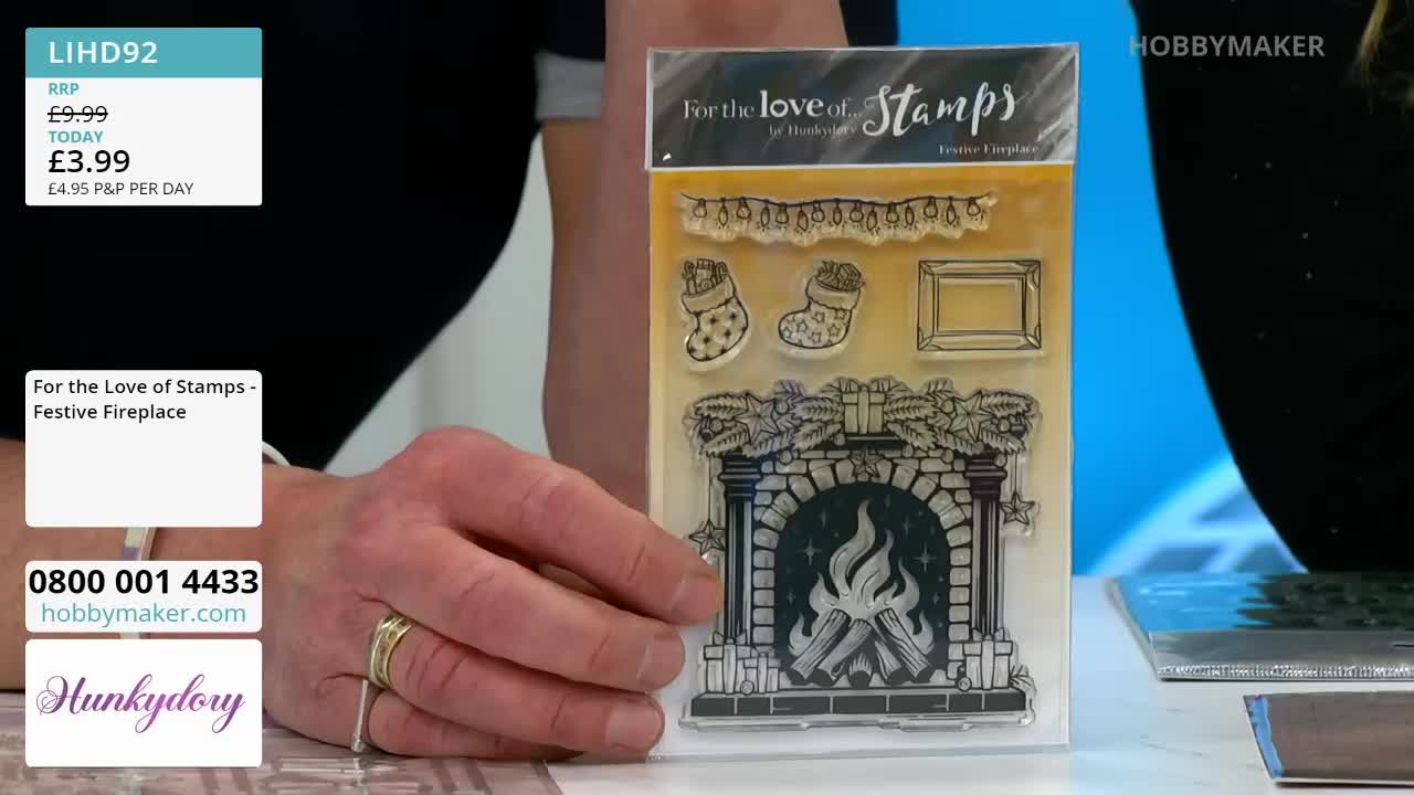 A hand holds a clear sheet of stamps featuring a festive fireplace design. The stamps include stockings, a picture frame, and a garland of lights.