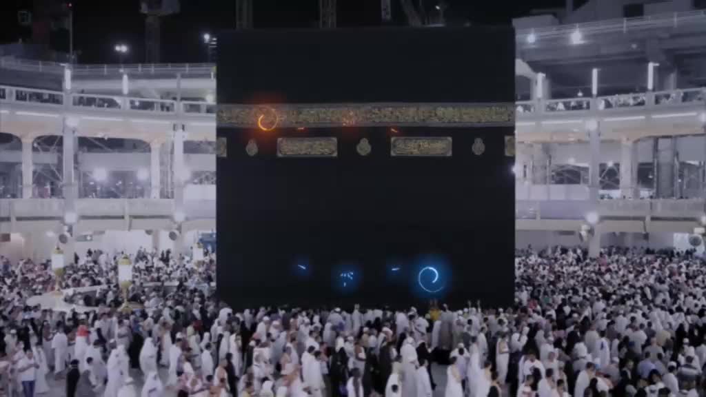 A large, black structure stands center, surrounded by a sea of people. Glowing, circular effects float near the building's surface.
