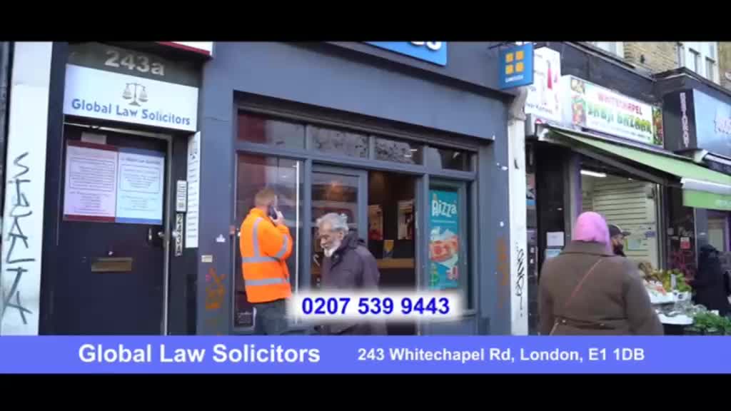 A man in an orange vest talks on his phone outside a law firm. Across the street, a person in a pink head covering walks past a shop with a green awning.
