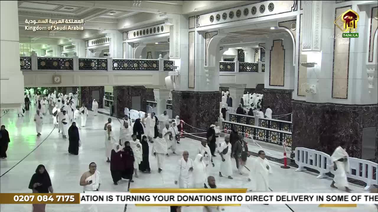 Pilgrims in white garments are walking through a grand, marble-clad hall. The broadcast from Iqra TV in the United Kingdom is showing a live feed of the scene.
