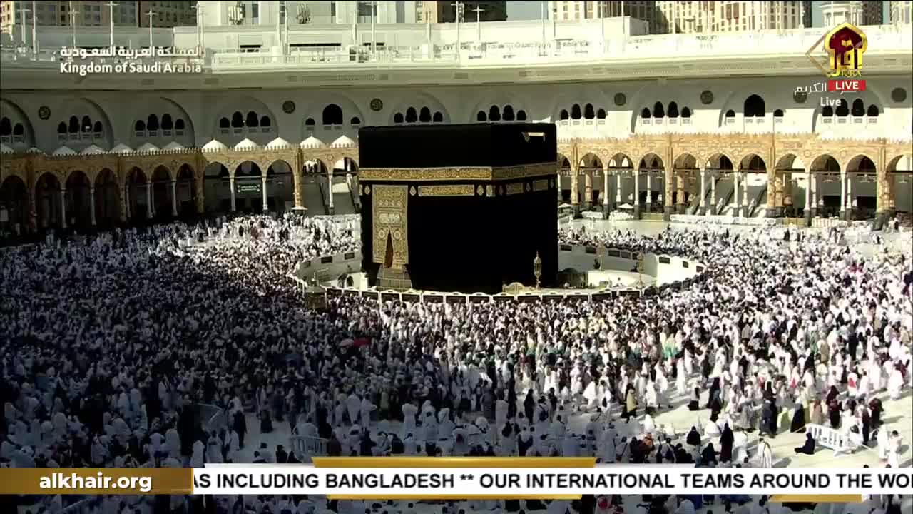 A sea of white-clad figures flows around the black Kaaba, the central focus of the scene. The live broadcast on Iqra TV from the United Kingdom captures the continuous movement of pilgrims.
