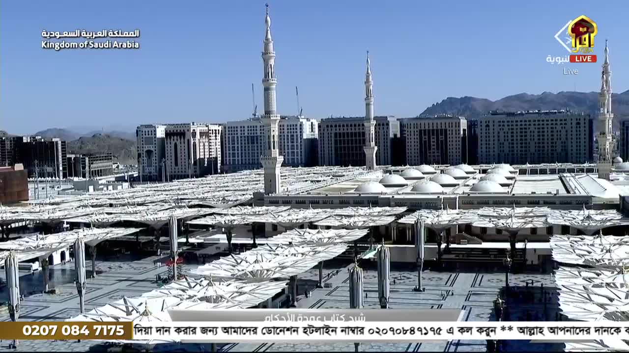 From this angle, I see a sprawling complex with towering minarets and a sea of white canopies. The broadcast, likely from Iqra TV in the United Kingdom, shows a live feed of the scene, with a call to donate at the bottom.
