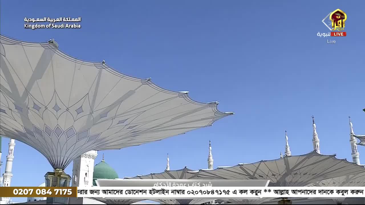 Massive, patterned white canopies are stretched across the sky, casting intricate shadows. The scene is broadcast live on Iqra TV from the Kingdom of Saudi Arabia.
