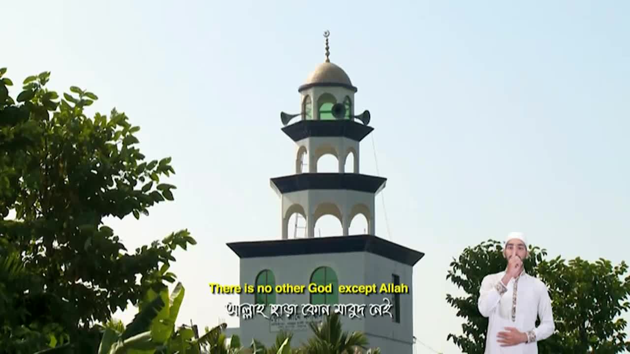 A man in a white cap and robe gestures near a tall minaret, with text from Iqra TV displayed on the screen. The tower's dome is topped with a crescent moon, and the sky is clear.
