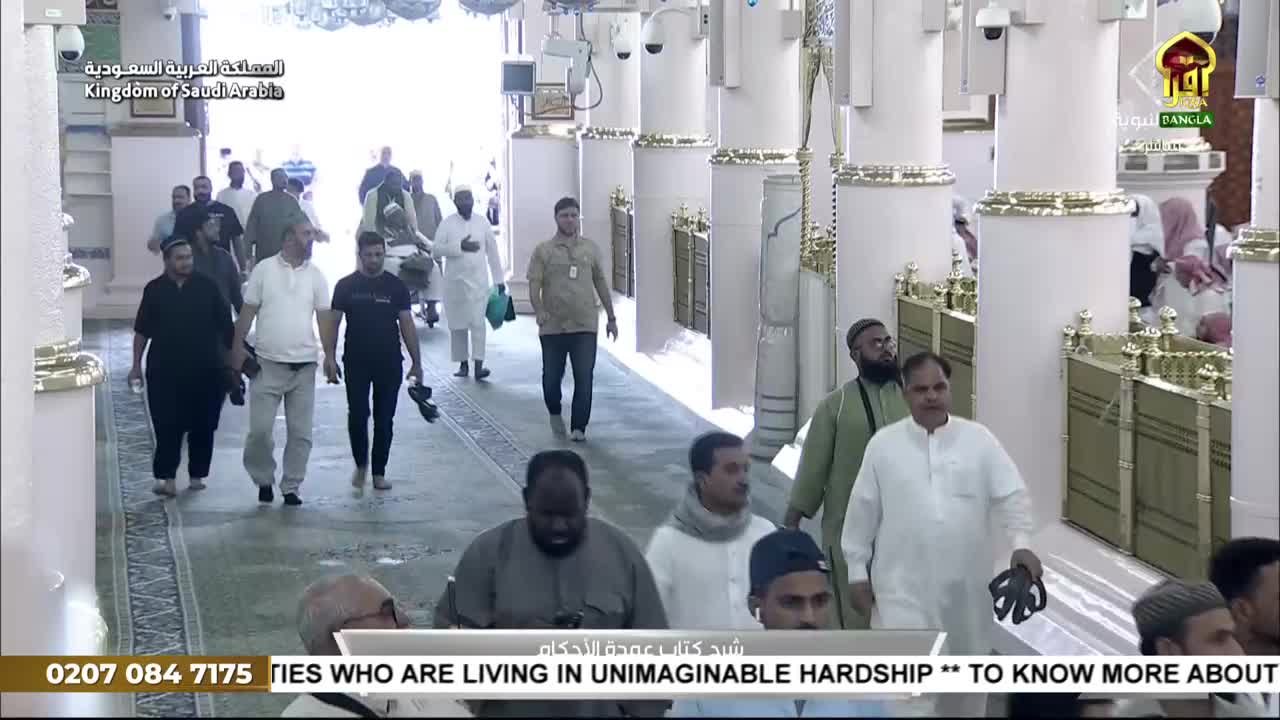 People are walking through a colonnade, some carrying bags or shoes. The broadcast from Iqra TV in the United Kingdom shows the scene, with a call for donations at the bottom of the screen.
