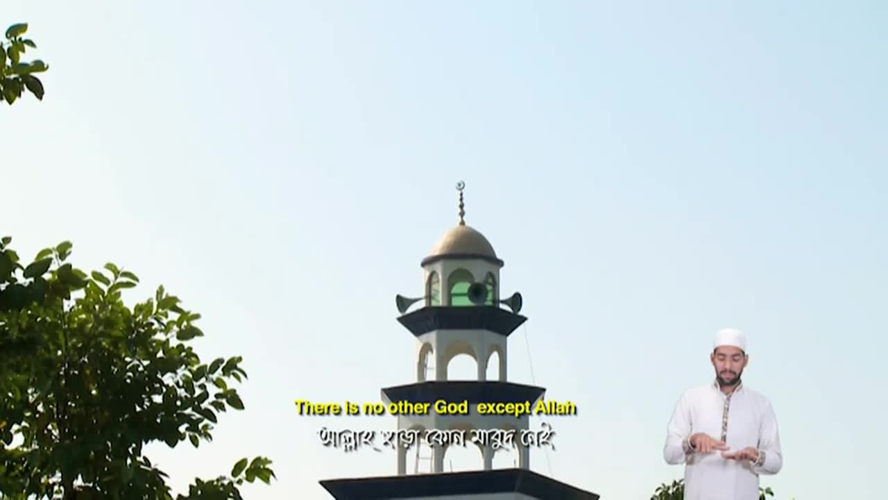 A man in a white cap and tunic stands below a mosque minaret, reading from a small book. Subtitles on Iqra TV in the United Kingdom display the words "There is no other God except Allah."
