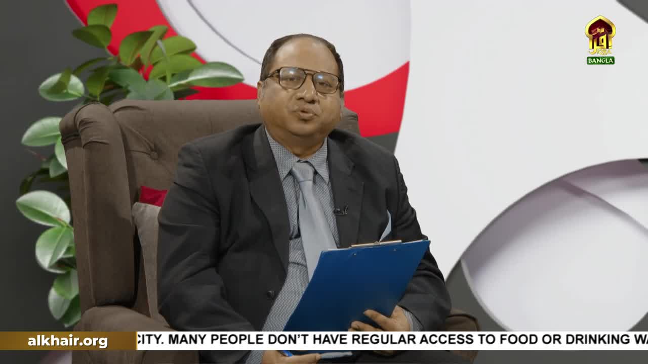 A man in a suit sits in a brown armchair, speaking directly into the camera. He holds a blue clipboard, and behind him, the Iqra TV Bangla logo is visible.
