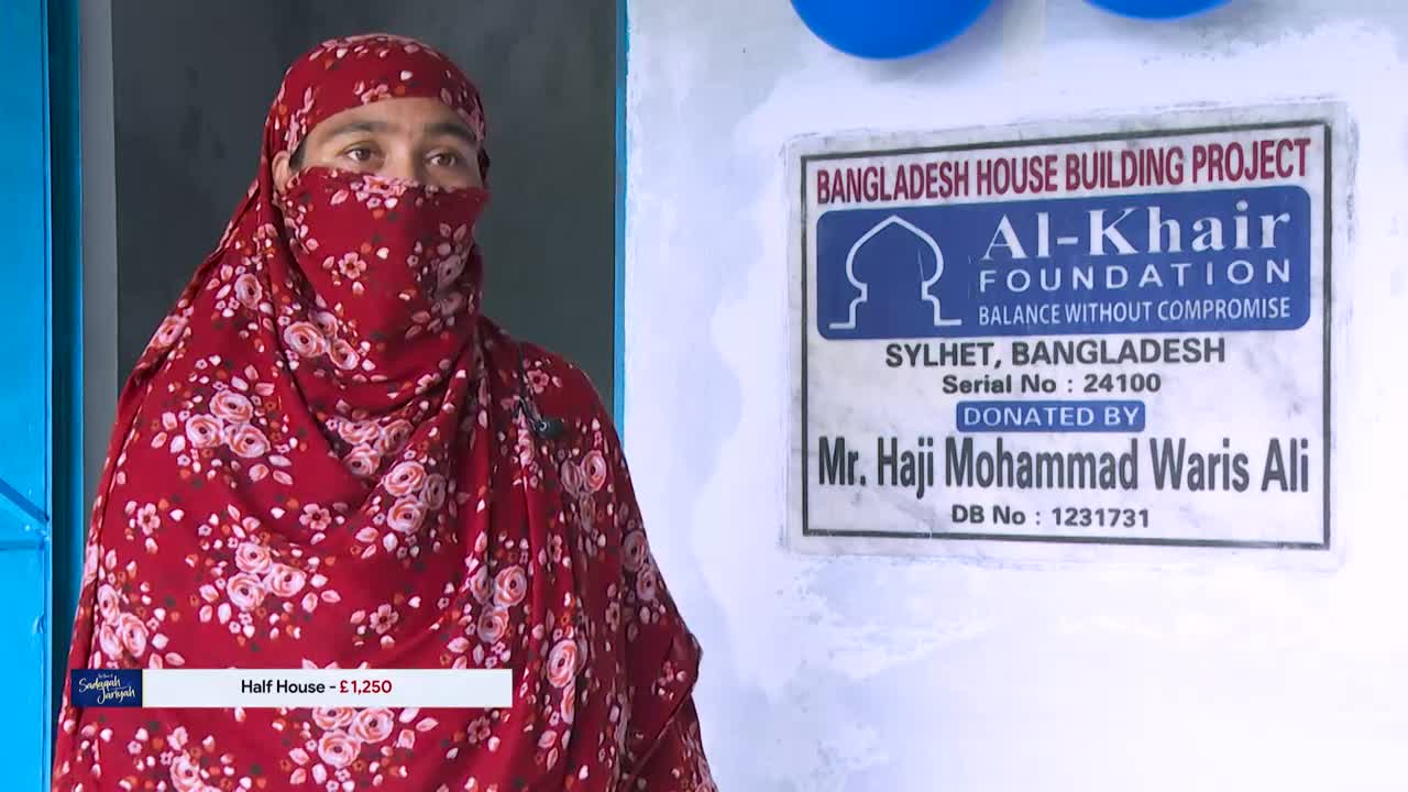 A woman in a red floral head covering stands next to a sign for the Al-Khair Foundation's Bangladesh House Building Project. The Iqra TV logo is visible in the corner, with a price for a "Half House" listed below.
