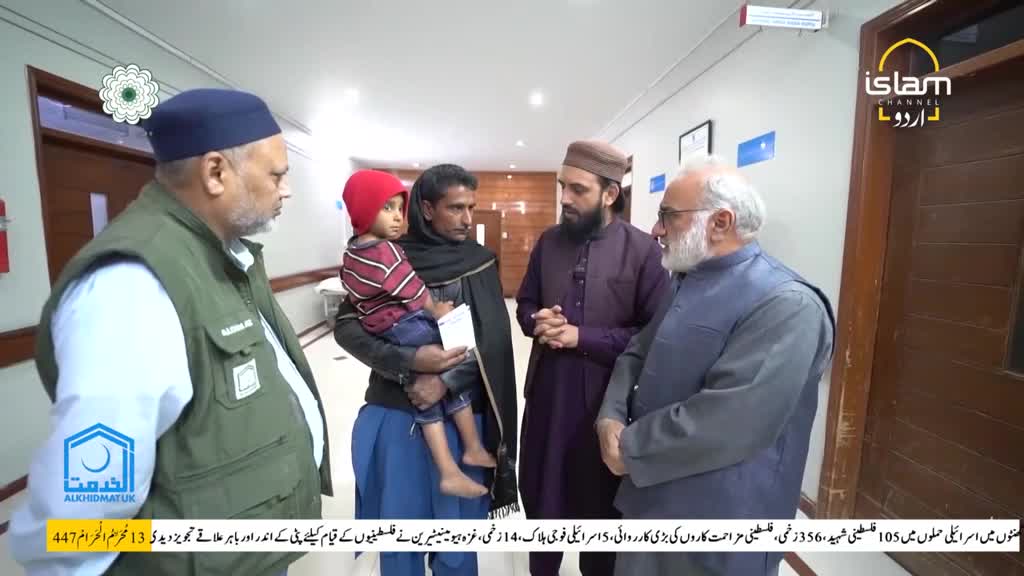 A man in a black shawl holds a child wearing a red hat, speaking with a group of men in a hallway. The Islam Channel Urdu logo is visible in the corner of the frame.
