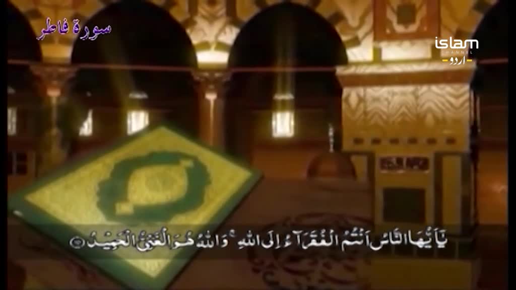 The Islam Channel Urdu logo is visible in the corner, as the camera focuses on a green and gold illuminated text. The scene appears to be a broadcast from a religious site, with Arabic script displayed on a screen. 
