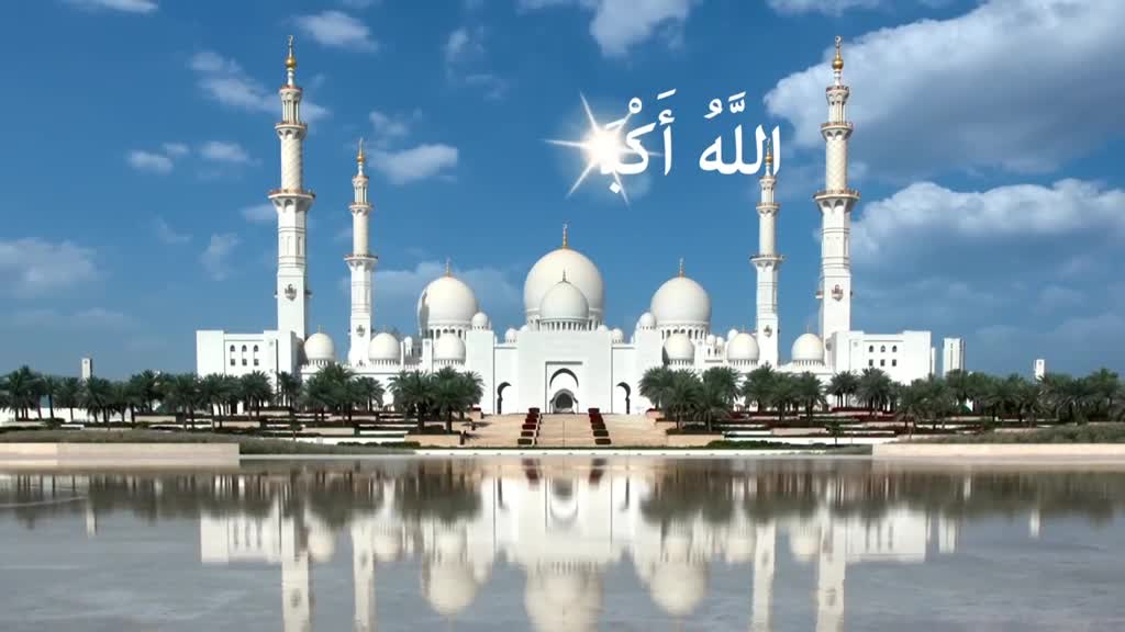 The white mosque, with its minarets reaching towards the sky, reflects perfectly in the still water. Above, the Arabic script gleams, catching the sunlight on a bright, clear day.
