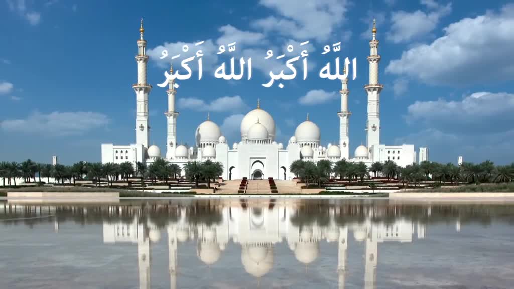 A grand white mosque, its minarets reaching towards a bright blue sky, is perfectly reflected in the still water. The Arabic script floats above the building, a reminder of the message broadcast on Islam Channel Urdu in the United Kingdom.
