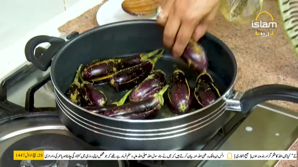 A hand is placing a coated eggplant into a pan, joining the others already cooking. The scene unfolds in a kitchen, likely part of a cooking segment from Islam Channel Urdu, based in the United Kingdom.
