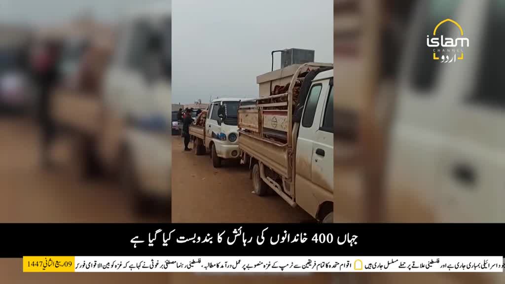 Several white pickup trucks are parked on a dirt road, with what looks like cargo in their beds. A few people in dark clothing are standing around the trucks, possibly overseeing something.
