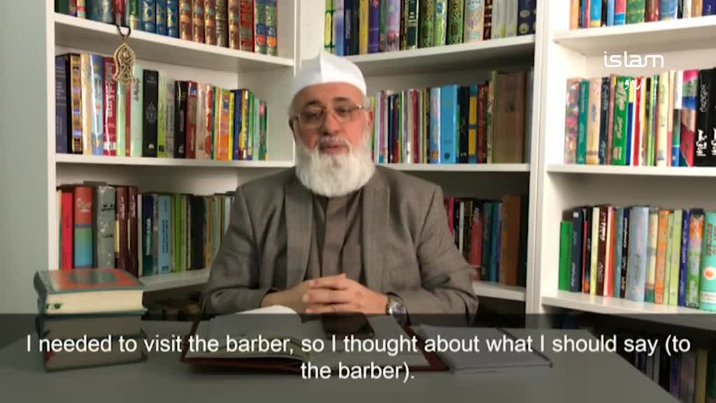 A man with a long white beard and a white cap is seated at a desk, speaking to the camera. Behind him, shelves are filled with books, and the logo for Islam is visible on the right.
