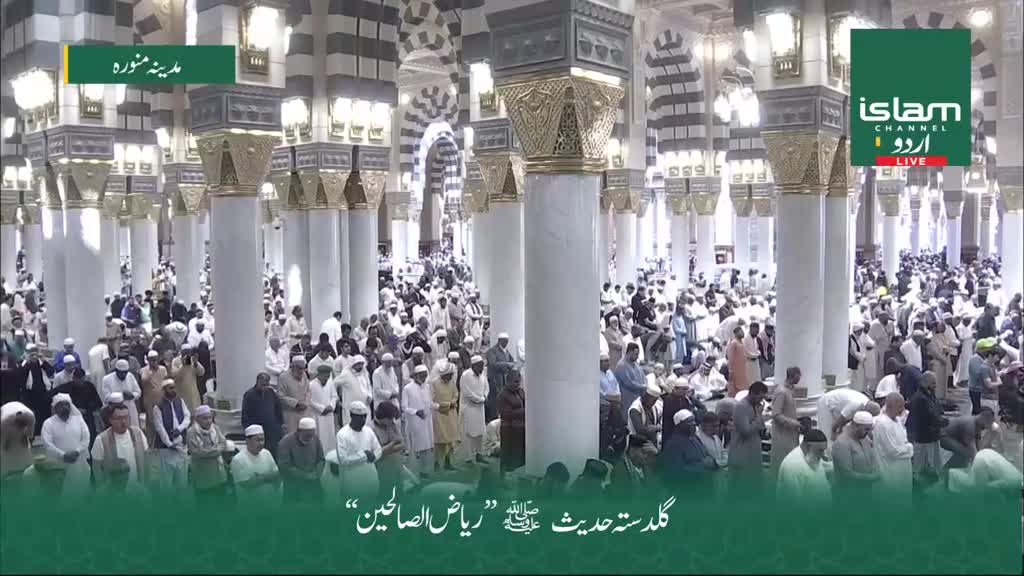 A large crowd of people, many wearing white, are gathered in a grand, pillared hall. The scene is broadcast live on Islam Channel Urdu from a location in Madinah.

